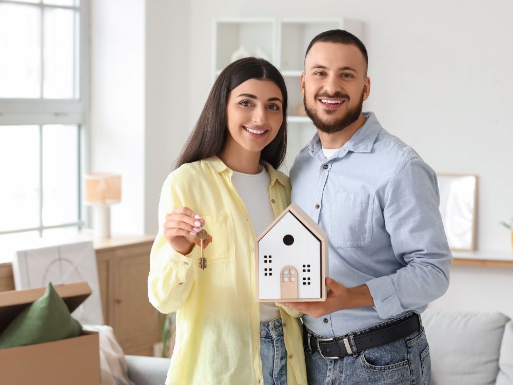 Casal segurando chave e maquete de casa nova, representando como funciona o aluguel sem fiador na conquista do imóvel.