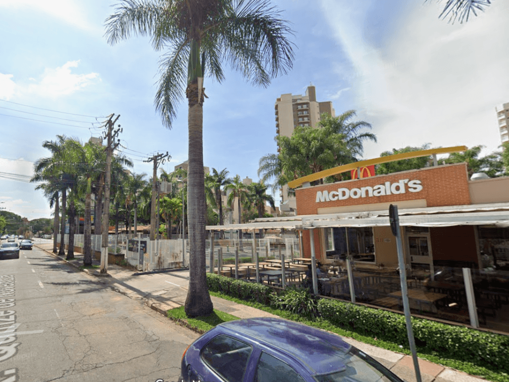 Rua arborizada com restaurante McDonald's, palmeiras e edifícios residenciais ao fundo, em uma área urbana de Indaiatuba.