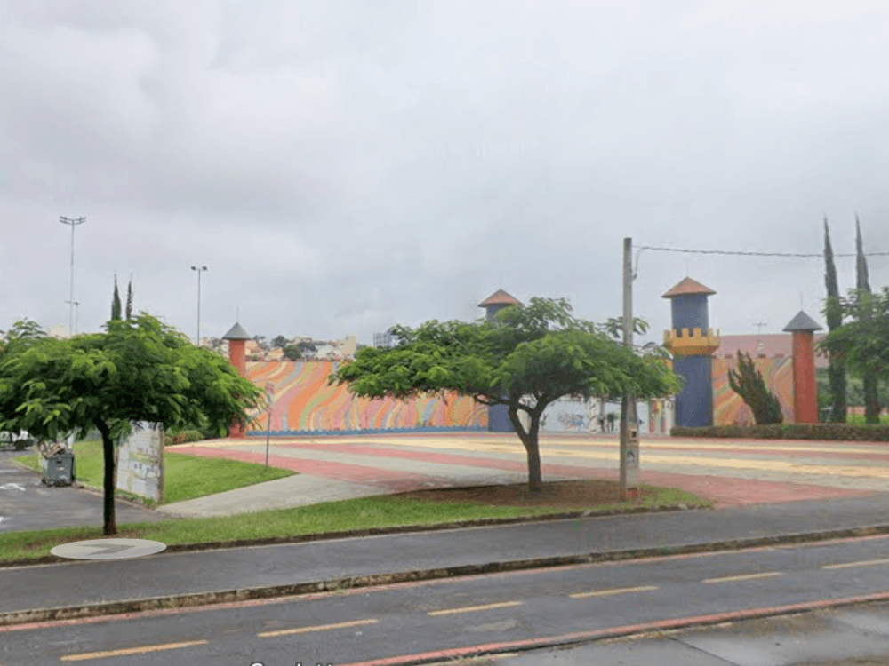 Área de lazer ao ar livre com árvores, quadra ampla e estruturas coloridas, ideal para atividades e passeios em Indaiatuba.