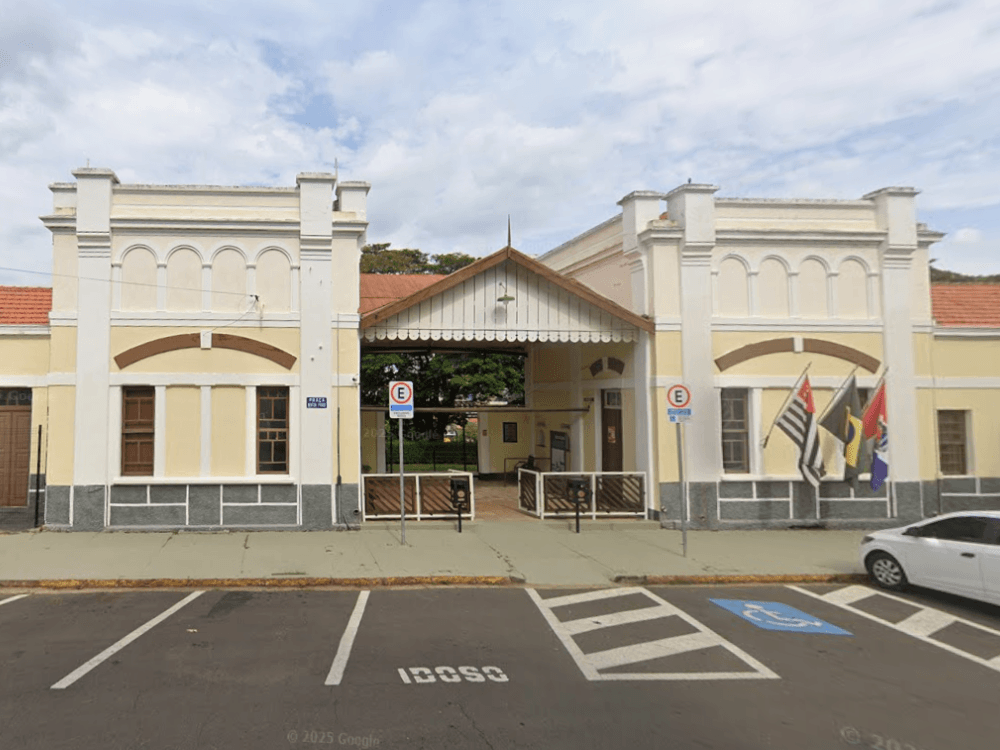 Prédio histórico com fachada clara, entrada central, bandeiras e área de estacionamento, um ponto de visita em Indaiatuba.