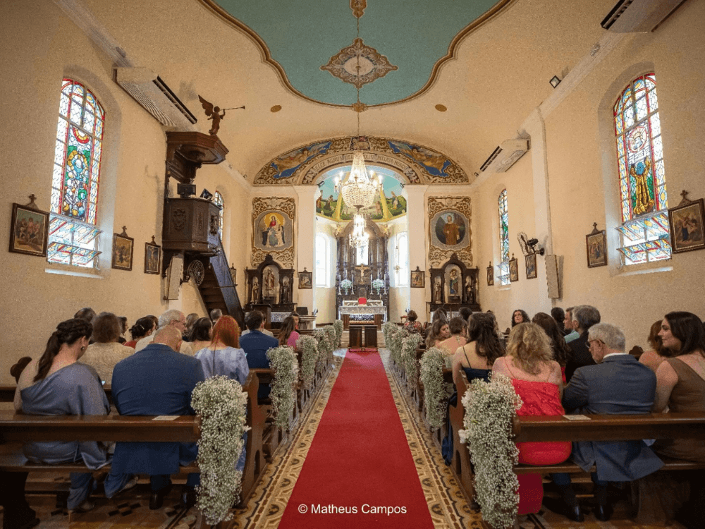Interior de igreja histórica no Bairro Helvetia em Indaiatuba, com vitrais, altar decorado e visitantes durante cerimônia