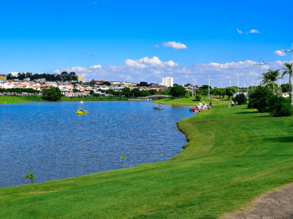 Lago cercado por área verde em Indaiatuba, com pessoas em pedalinhos e moradores aproveitando o espaço ao ar livre. Tudo para mostrar opções de lazer em Indaiatuba